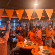 Groep bezoekers in oranje kleding viert samen tijdens een voetbalavond.