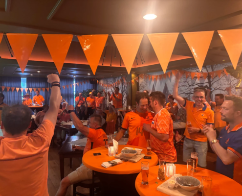 Groep bezoekers in oranje kleding viert samen tijdens een voetbalavond.