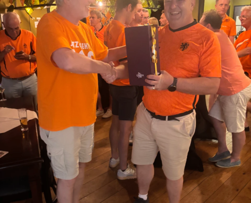 Twee mannen in oranje kleding schudden elkaar de hand tijdens een prijsuitreiking.